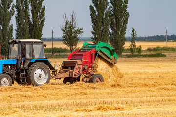 tractor makes big straw roll on yellow field at summer day