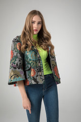 young blonde model posing in stylish flower pattern jacket and neon green blouse. blue jeans. white background. 