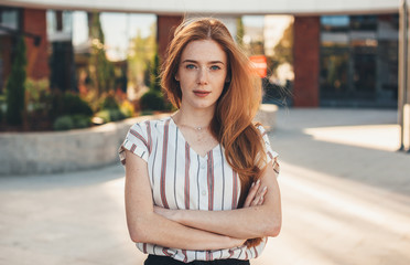 A nice picture of a gorgeous red haired woman looking confident and posing outside in front of a...