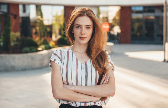 A nice picture of a gorgeous red haired woman looking confident and posing outside in front of a big company