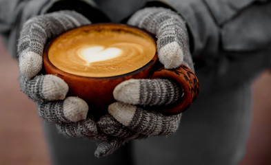 female hands in gloves hold a cup of hot cappuccino coffee on the street