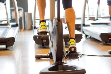 Athletic man cycling on stationary bike in gym. Focus on leg.