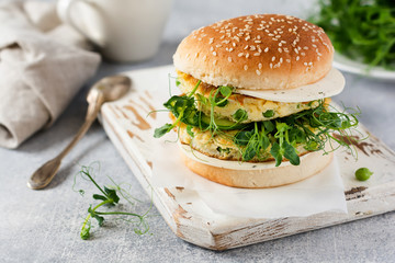 Healthy Vegetarian burger with egg and pea shoots and seeds microgreen, fresh salad, cucumber slice on a cutting wooden board on light background. Selective focus.