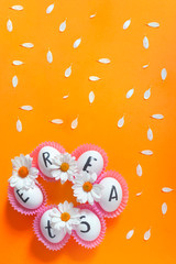 Bright Easter image with fresh spring flowers on the orange background. White eggs with text - Easter on the bright colorful background