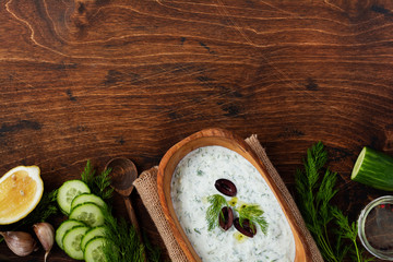 Traditional Greek sauce Tzatziki in olive wooden bowl on old rustic background. Top view.