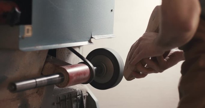 Traditional bespoke shoemaker shaping grinding leather insole on wooden shoe last with sand grinder machine