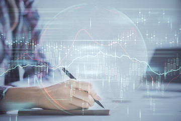 A woman hands writing information about stock market in notepad. Forex chart holograms in front. Concept of research. Double exposure