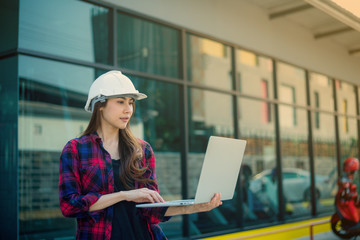 A female engineer is analyzing the building structure plan on a portable computer and she is feeling the heat from the air in front of the construction project.