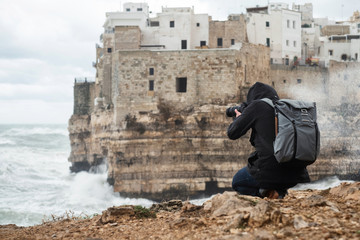 Fototapeta na wymiar Photographer taking picture of a stormy sea in Polignano a Mare, Italy