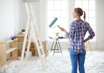 Beautiful young woman doing wall painting, standing near ladder