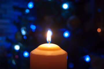 A burning orange candle on a dark background with blue lights - a Christmas New Year's eve divination mystic esoteric romance love mood. Horizontal photo, side, focus or defocus