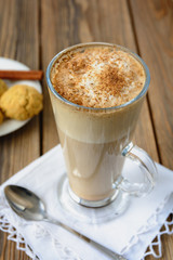 Homemade latte coffee with cinnamon on a white napkin next to spoon on a wooden table