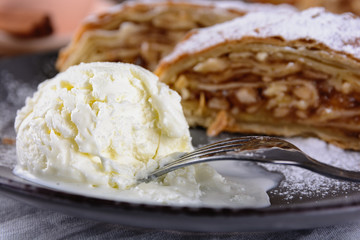 Ice cream ball and  delicious strudel stuffed with apples and cinnamon at a plate, close up