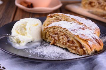 Pair pieces of delicious strudel stuffed with apples and cinnamon at a plate next to ice cream ball