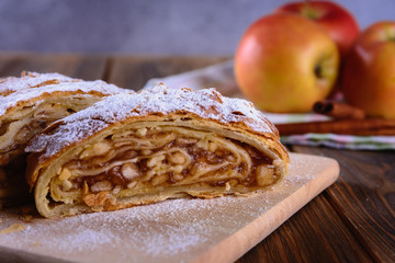 Delicious strudel stuffed with apples and cinnamon and red apples on background
