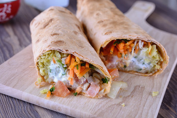 Appetizing rolls with meat and vegetable filling, as shawarma or burrito on a wooden desk are ready to eat, close up