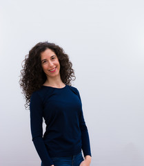 Obraz premium young pretty woman with black curly hair looking happy, cheerful and confident, smiling proudly and looking to side against white wall.