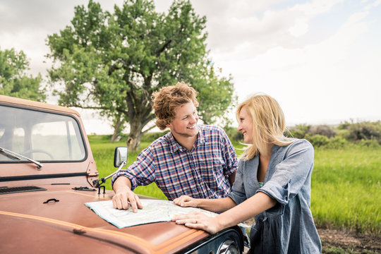 Young couple driving through the hills with an old jeep, reading a map. Bridger, Montana, USA