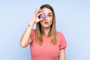 Young blonde woman over isolated blue background holding colorful French macarons with funny face