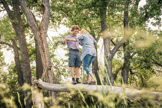 Young couple hanging out and having a fun picnic in a park, balancing on log. Bridger, Montana, USA