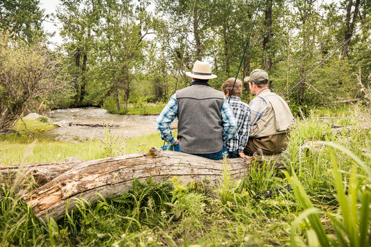 Grandfather, father and grandson sitting on log next to stream. Red Lodge, Montana, USA