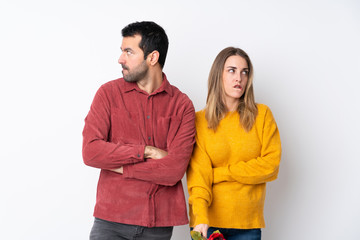 Couple in Valentine Day holding flowers over isolated background with confuse face expression while bites lip