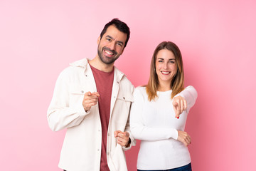 Couple in Valentine Day over isolated pink background points finger at you with a confident expression