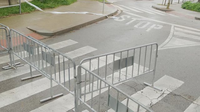 Pedestrian crossing closed by fences. Police blocked a crosswalk due to a hurricane and flood. City road with pedestrian crossing. Strong wind moves ragged ribbons. 