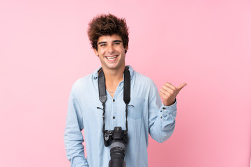 Young caucasian man over isolated pink background with a professional camera and pointing to the...