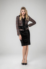 sexy blonde model posing in shiny chic gray suit. black handbag. white background. standing. studio shot.