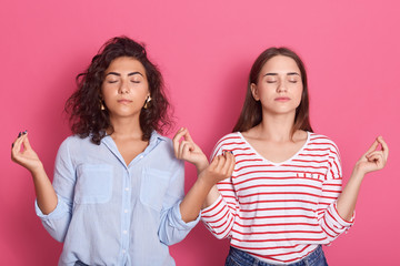 Close up portrait of calm girl wearing casual clothing, relaxing, meditating, breathes deeply with mudra om and shut eyes, isolated over on pink background, brunette females standing together.