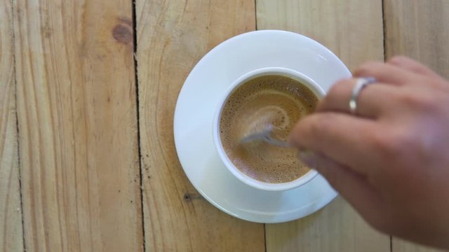 Top view of Person hand steering coffee in a cup with spoon. Breakfast morning of a cup hot black coffee on wooden background. footage b-roll scene 4k. home making coffee.