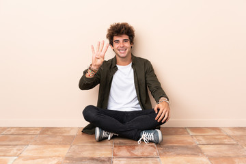 Young caucasian man sitting on the floor happy and counting four with fingers