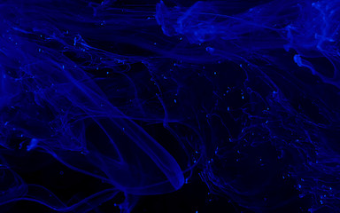 Blue watercolor ink in water on a black background. Colored space magic background.
