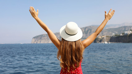 Beautiful young woman with hat and raised arms looking at stunning panoramic village of Sorrento on...