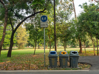 Fototapeta na wymiar The multicoloured trash bins with the signs for waste separation, like plastic, cans, bottles and other and a walking lane sign are placed in the public park.