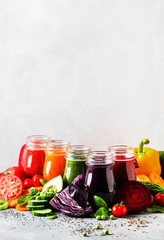 Colorful vegan vegetable juices and smoothies selection in bottles on gray kitchen table, copy space