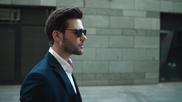 Side view businessman walking in suit. Man wearing sunglasses at street