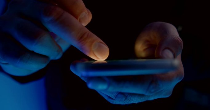 man is scrolling display of smartphone, browsing internet at night, closeup view of fingers