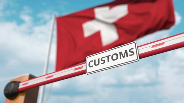 Closing boom barrier with CUSTOMS sign against the Swiss flag. Restricted border crossing or protective tariffs in Switzerland