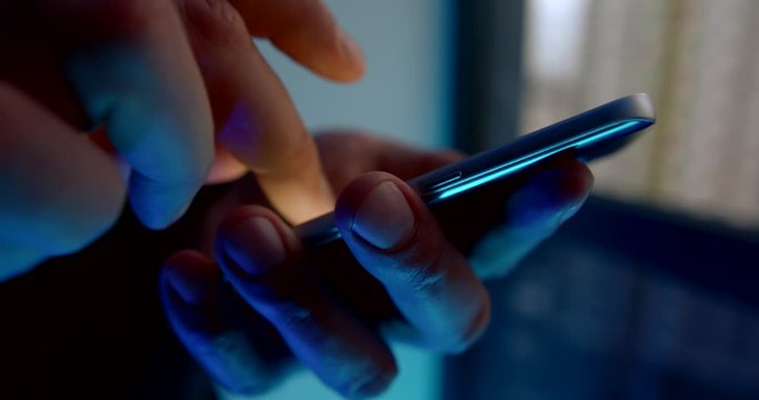 man is using mobile phone in darkness, tapping and swiping on screen, closeup