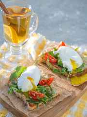 Poached egg on toast with arugula and cherry tomatoes for breakfast on paper and a wooden board with tea