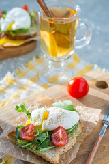 Poached egg on toast with arugula and cherry tomatoes for breakfast on paper and a wooden board with a fork. Vertical arrangement