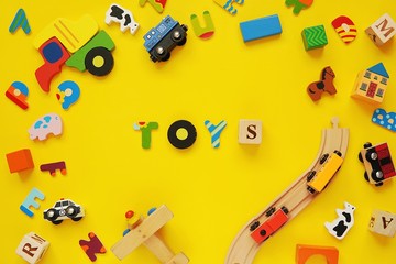 Word TOYS and frame with colorful wooden kids toys on yellow background.