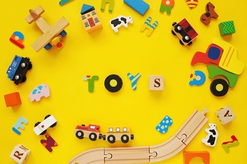 Word TOYS and frame with colorful wooden kids toys on yellow background.
