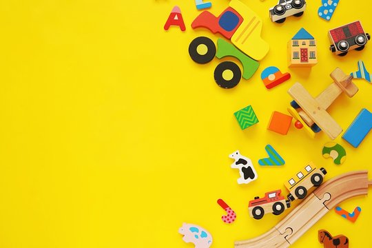 Set of colorful wooden kids toys, cars, trains, building blocks on yellow background.