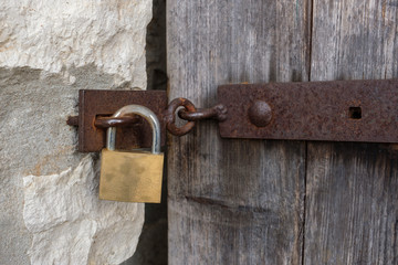 Ein Vorhängeschloss und ein rostiger Riegel an einer verwitterten Holztür