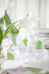 Obraz na płótnie Canvas Decor and table setting of the Easter table with white tulips and dishes of green and white color. Easter decor in the form of Easter bunnies green color with white polka dots.