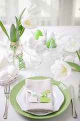 Decor and table setting of the Easter table with white tulips and dishes of green and white color. Easter decor in the form of Easter bunnies  green color with white polka dots.