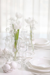 Happy Easter! Decor and table setting of the Easter table with white tulips and dishes of white color.